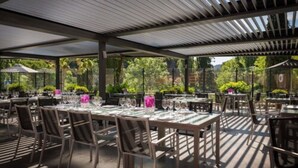 An outdoor dining area with tables set for two, covered by a metal roof, and surrounded by greenery. - Hostellerie Les Gorges de Pennafort (Callas)