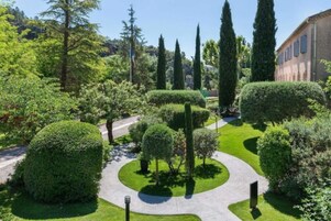 Un jardín bien cuidado con setos y árboles recortados, un camino despejado y un edificio al fondo.