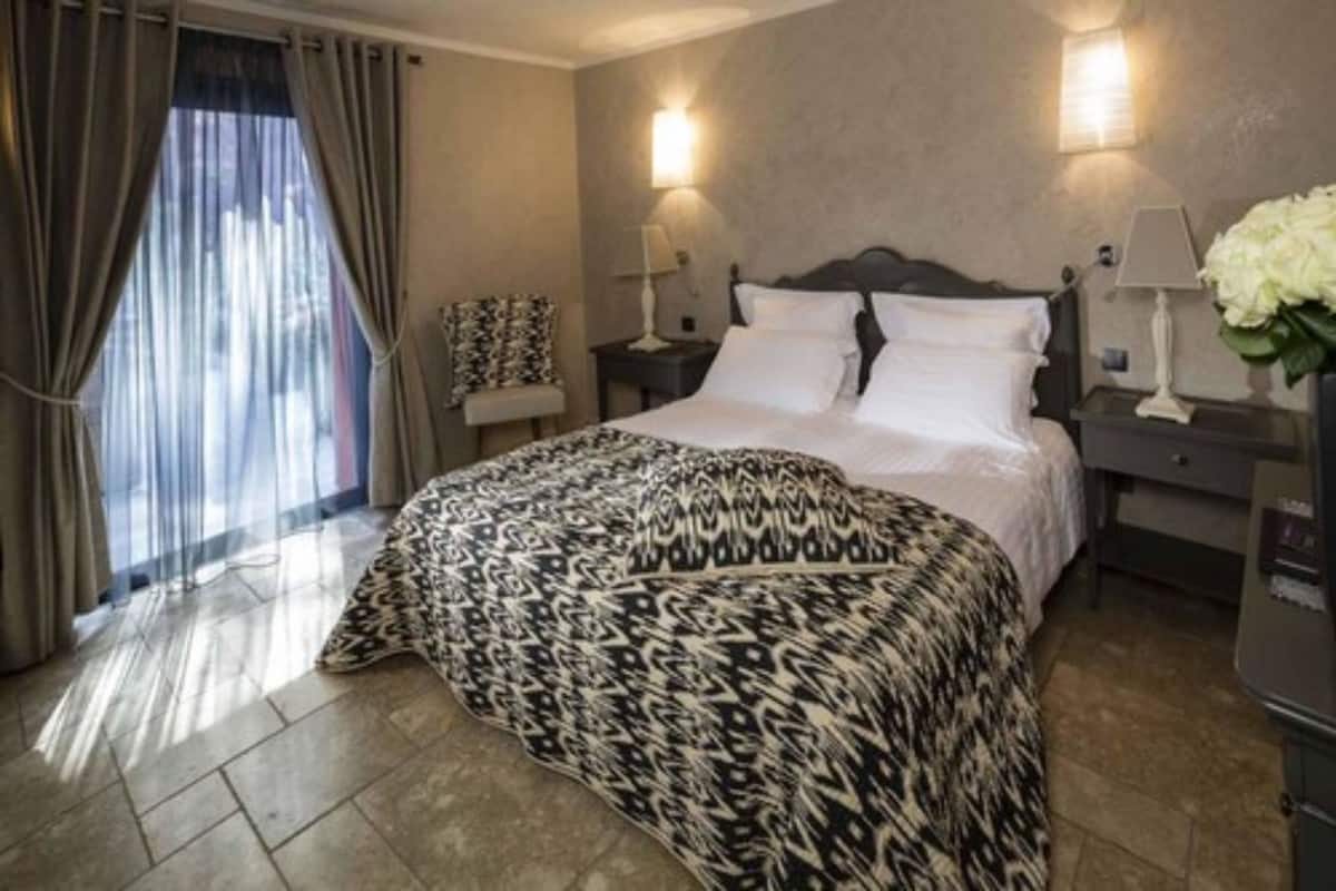 Habitación de hotel con cama, dos mesitas de noche con lámparas, un pupitre y una ventana con cortinas.