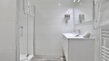 Un baño moderno con cabina de ducha de vidrio, un lavamanos blanco, un perchero y un secador de manos.