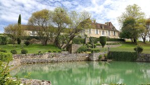 A serene pond with a stone bridge, surrounded by lush greenery and a large house with a stone wall and a well-maintained garden. - La Chartreuse du Bignac (Saint-Nexans)