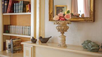 A bookshelf with books and decorative items, a mirror with a floral arrangement, and a small bird figurine on a dresser.
