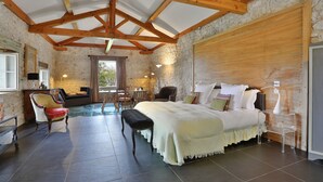 A bedroom with a large bed, wooden beams, stone walls, a bench, and a chair. - La Chartreuse du Bignac (Saint-Nexans)