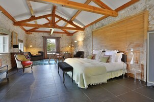 Un dormitorio con una cama grande, vigas de madera, paredes de piedra, un banco y una silla.