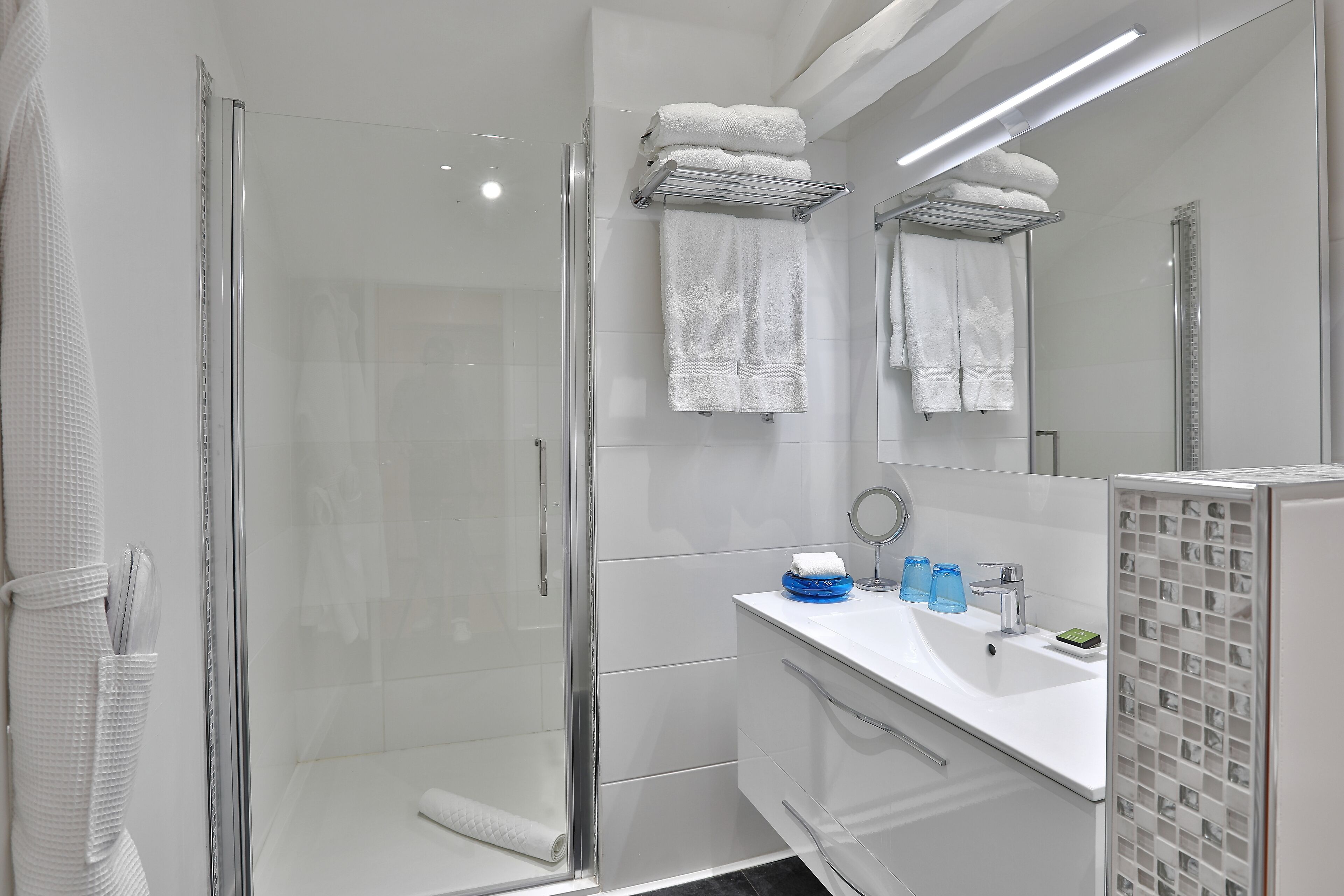 Une salle de bain moderne avec une douche à parois de verre, un lavabo blanc avec un miroir et un porte-serviettes avec des serviettes pliées.
