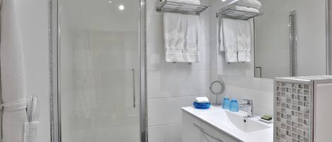 Une salle de bain moderne avec une douche à parois de verre, un lavabo blanc avec un miroir et un porte-serviettes avec des serviettes pliées.