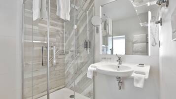 A modern bathroom with a glass-enclosed shower, a white sink with a mirror, and a towel hanging on the wall.