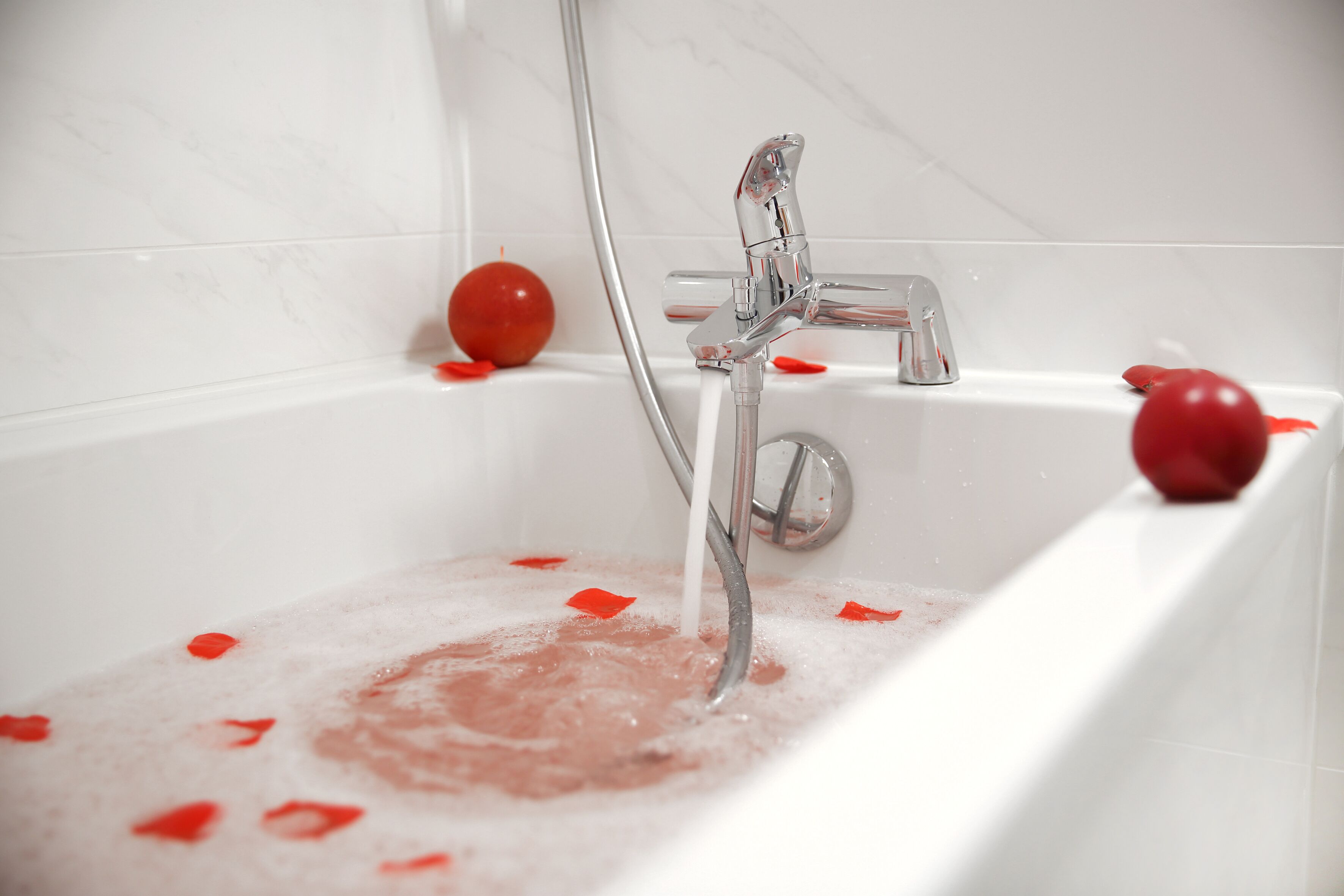Una bañera con pétalos de rosa y una rosa roja.