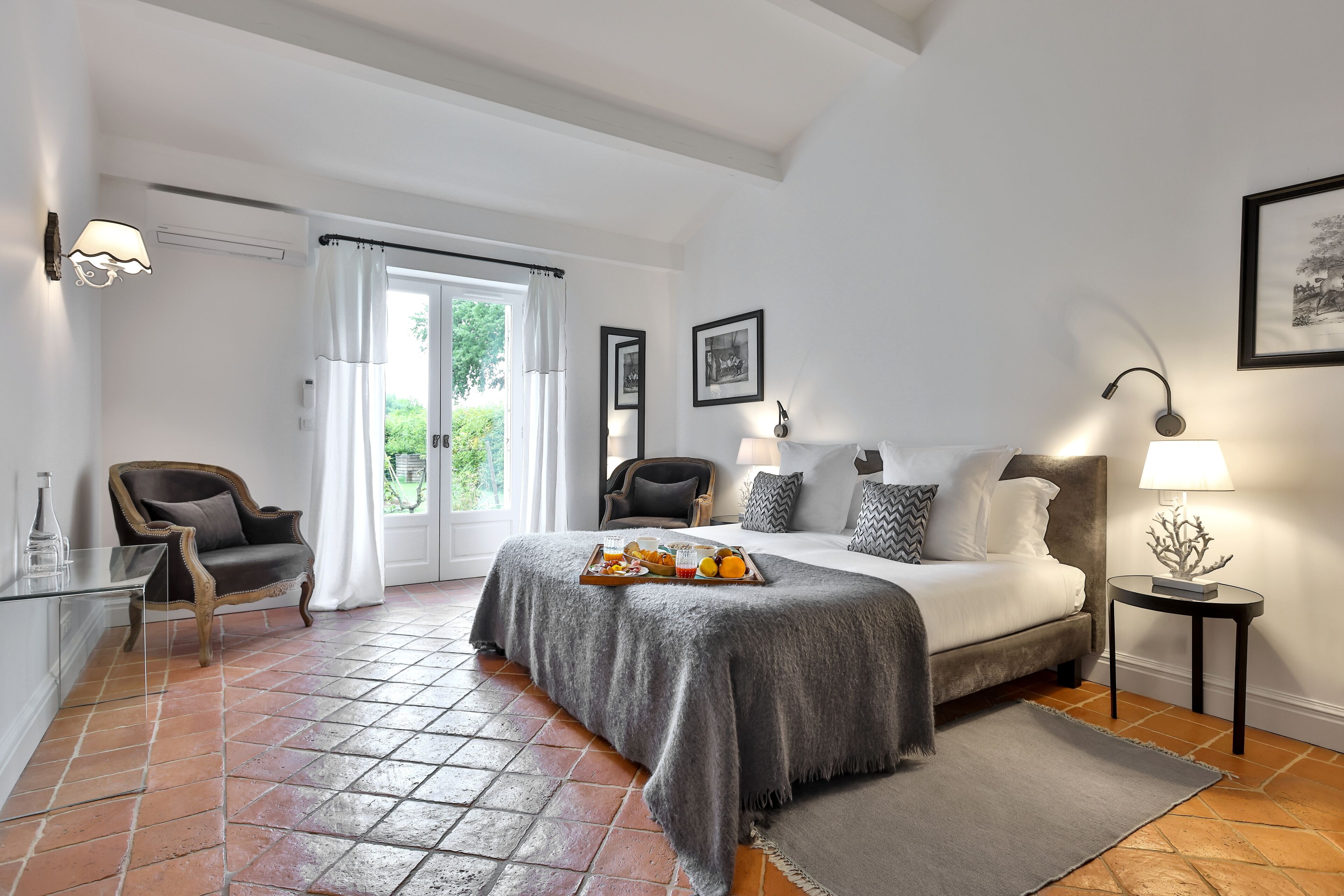 A bedroom with a bed, a chair, a table with a tray of fruit, a lamp, and a picture on the wall.