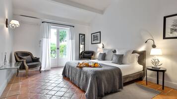 A bedroom with a bed, a chair, a table with a tray of fruit, a lamp, and a picture on the wall.