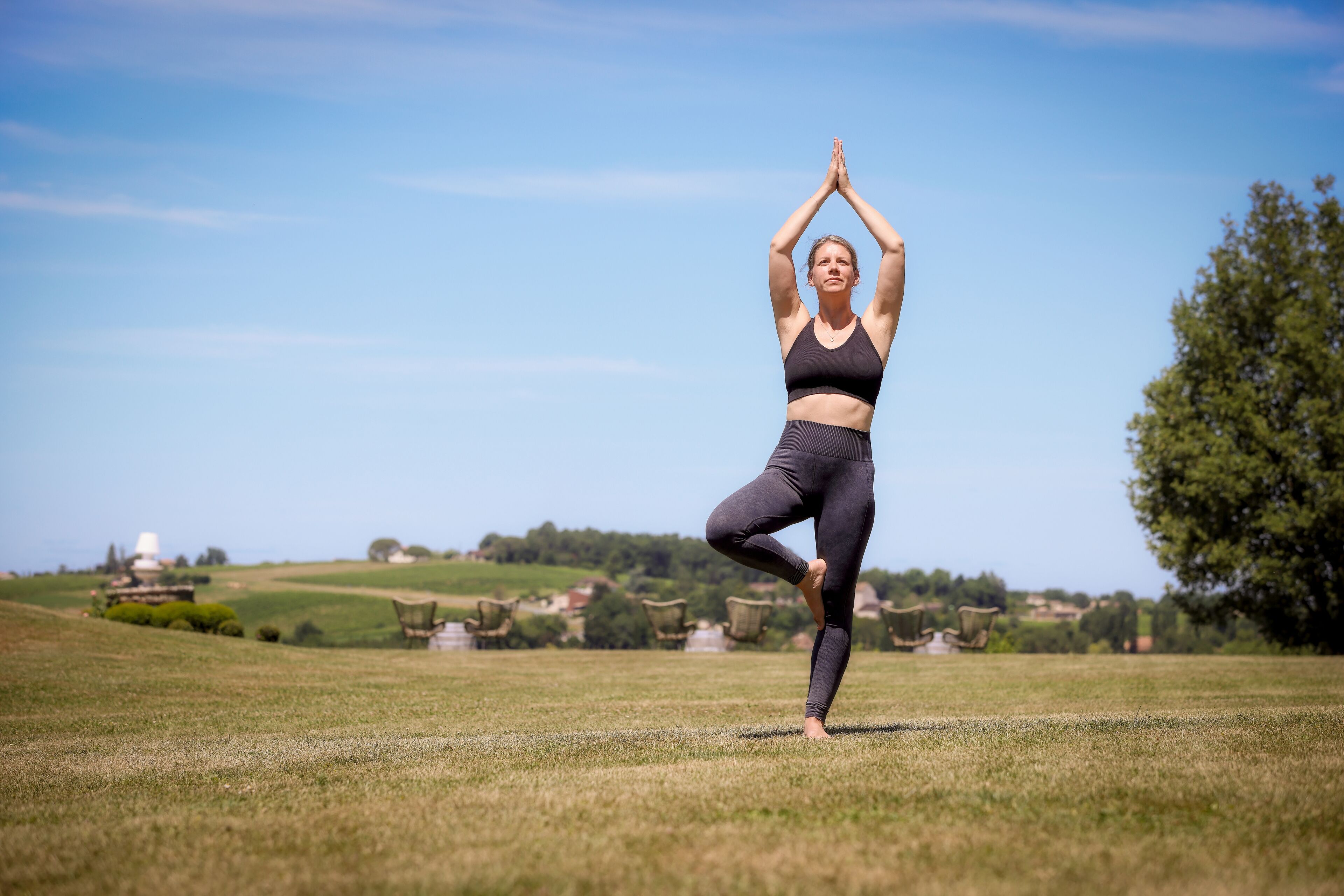 En person laver en yogastilling i en åben mark med klar himmel og fjerne bygninger.
