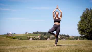 En person laver en yogastilling i en åben mark med klar himmel og fjerne bygninger.