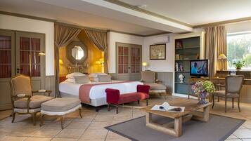 A hotel room with a large bed, two armchairs, a wooden coffee table, a television, and a bookshelf.