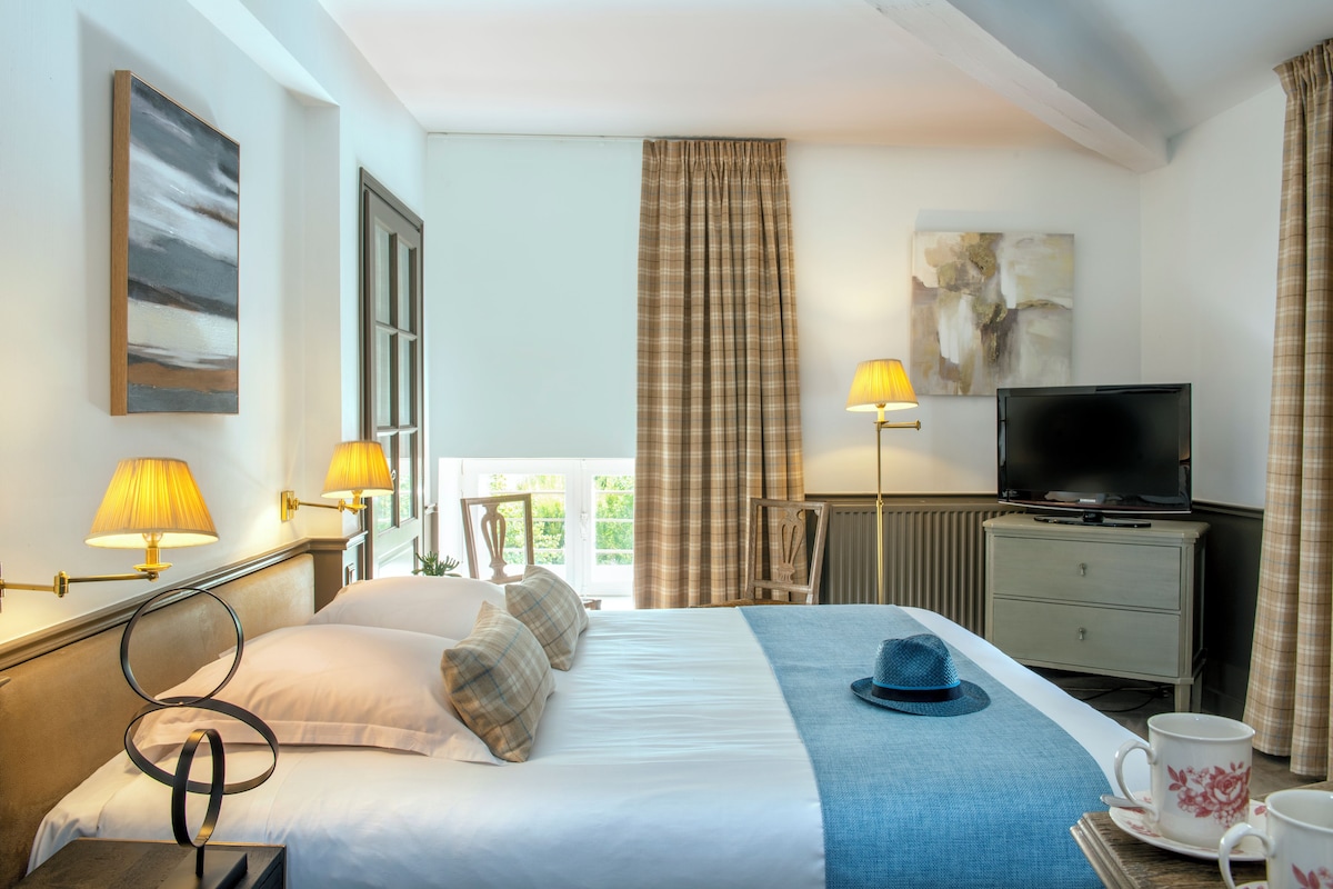 Una habitació d'hotel amb un llit, una televisió, una taula de nit amb una làmpada i una finestra amb cortines.
