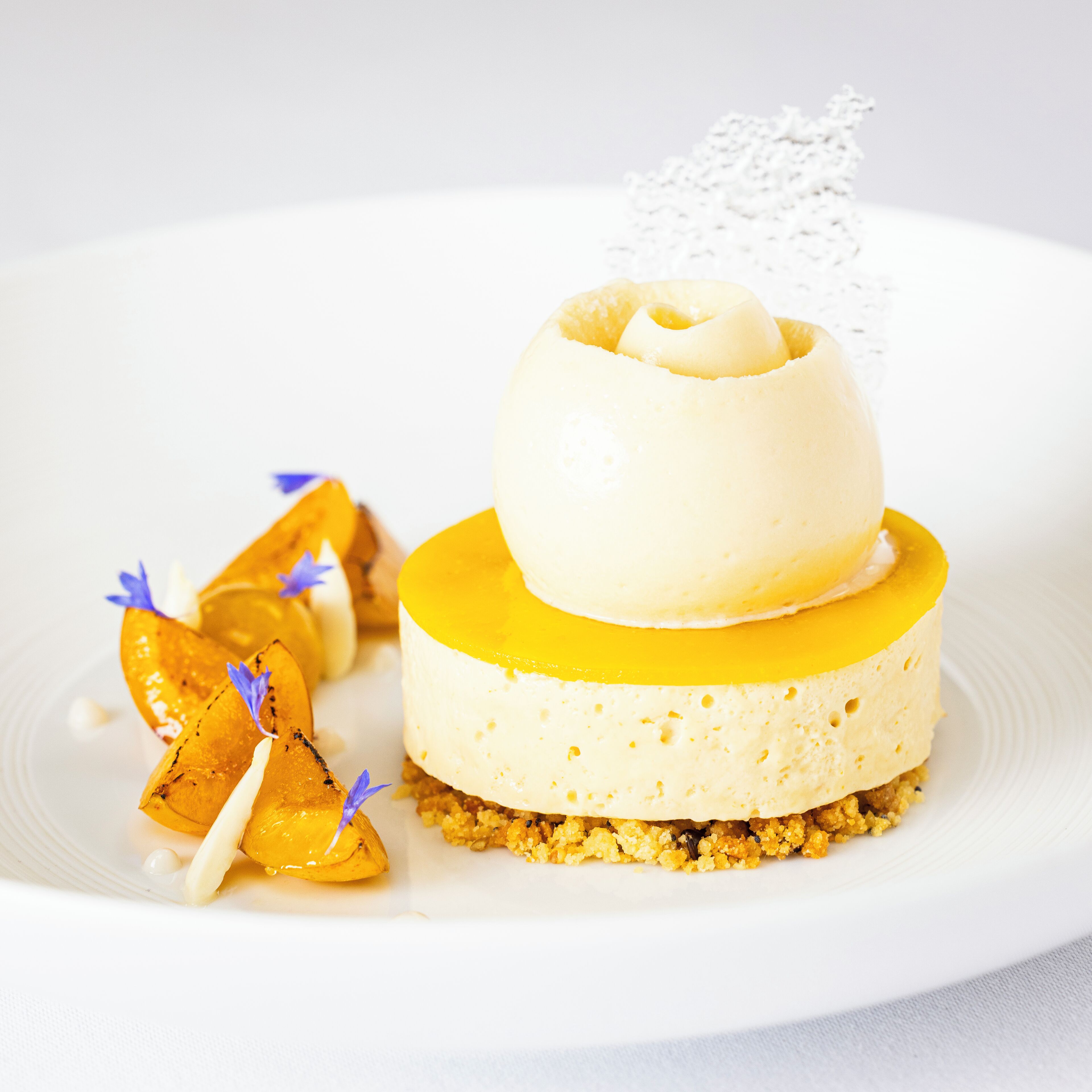A dessert with a yellow base, a white layer, and a top layer with a flower decoration.