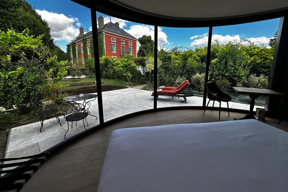 Ein Schlafzimmer mit einem großen Bett, einem gebogenen Fenster, einem kleinen Tisch und einem Sessel.