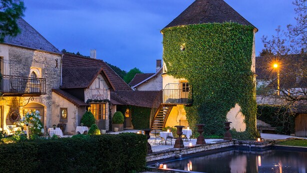 Un bâtiment historique doté d’une tour, d’une cour avec un bassin décoratif et d’espaces aménagés pour se détendre en plein air.