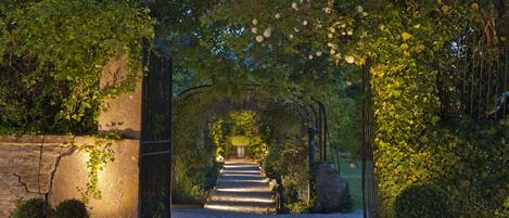 A pathway leading through a garden with a stone wall on one side and a metal gate on the other.