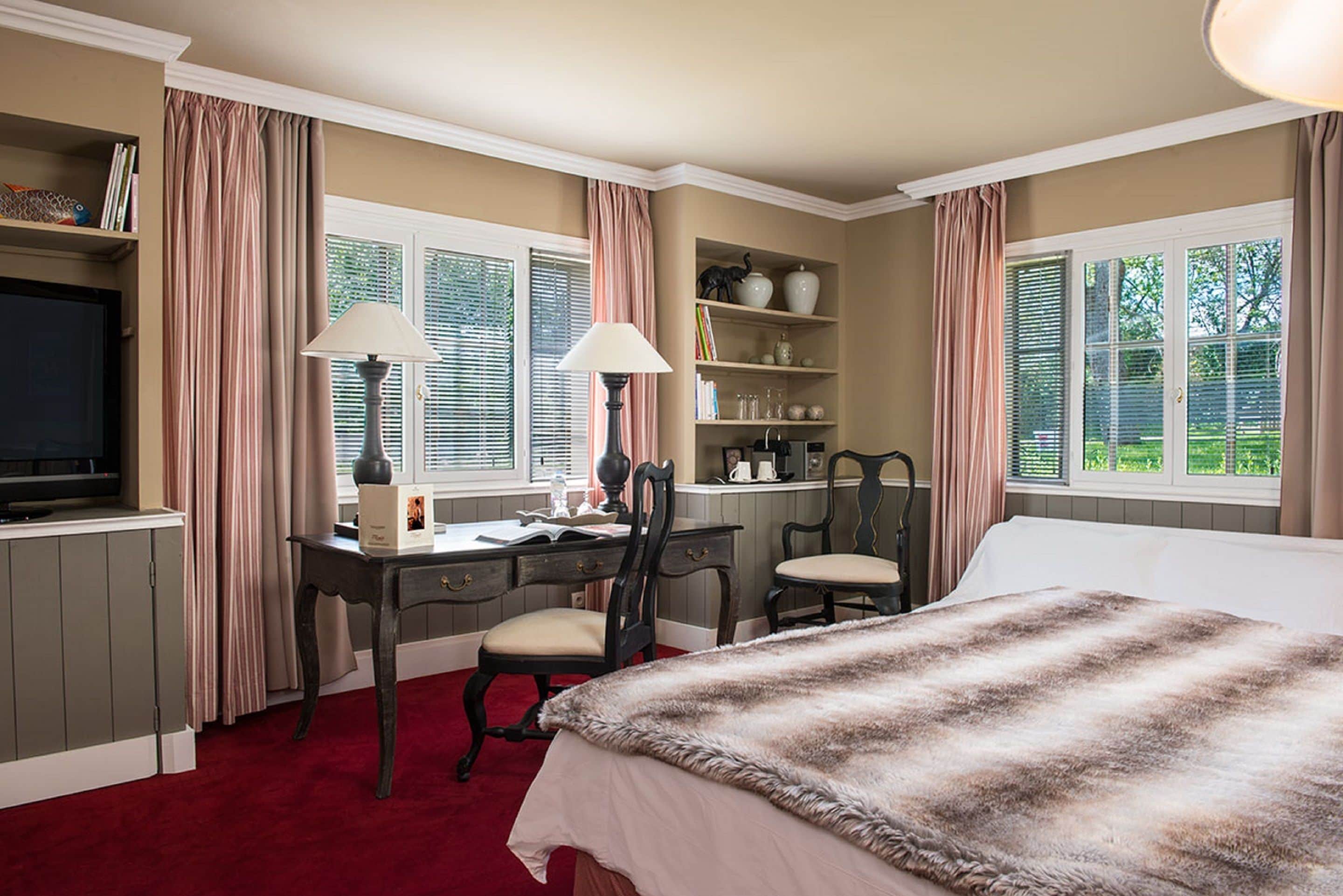 A bedroom with a bed, two chairs, a desk, and a television.