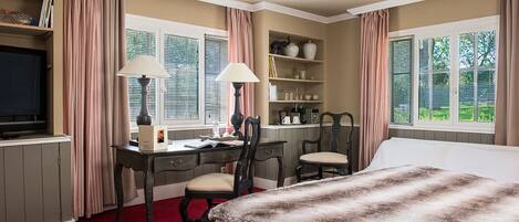 A bedroom with a bed, two chairs, a desk, and a television.