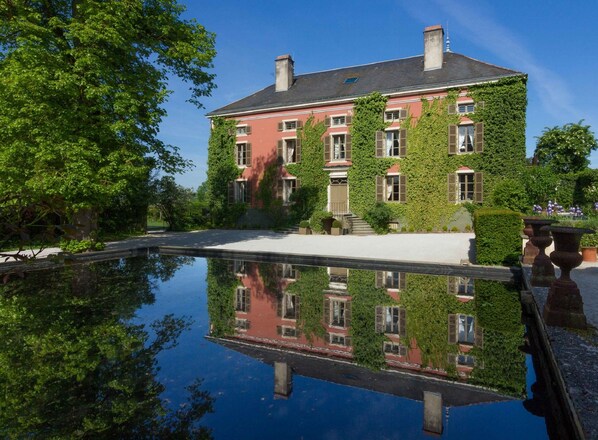 Um edifício grande coberto de hera com uma piscina refletora em frente.