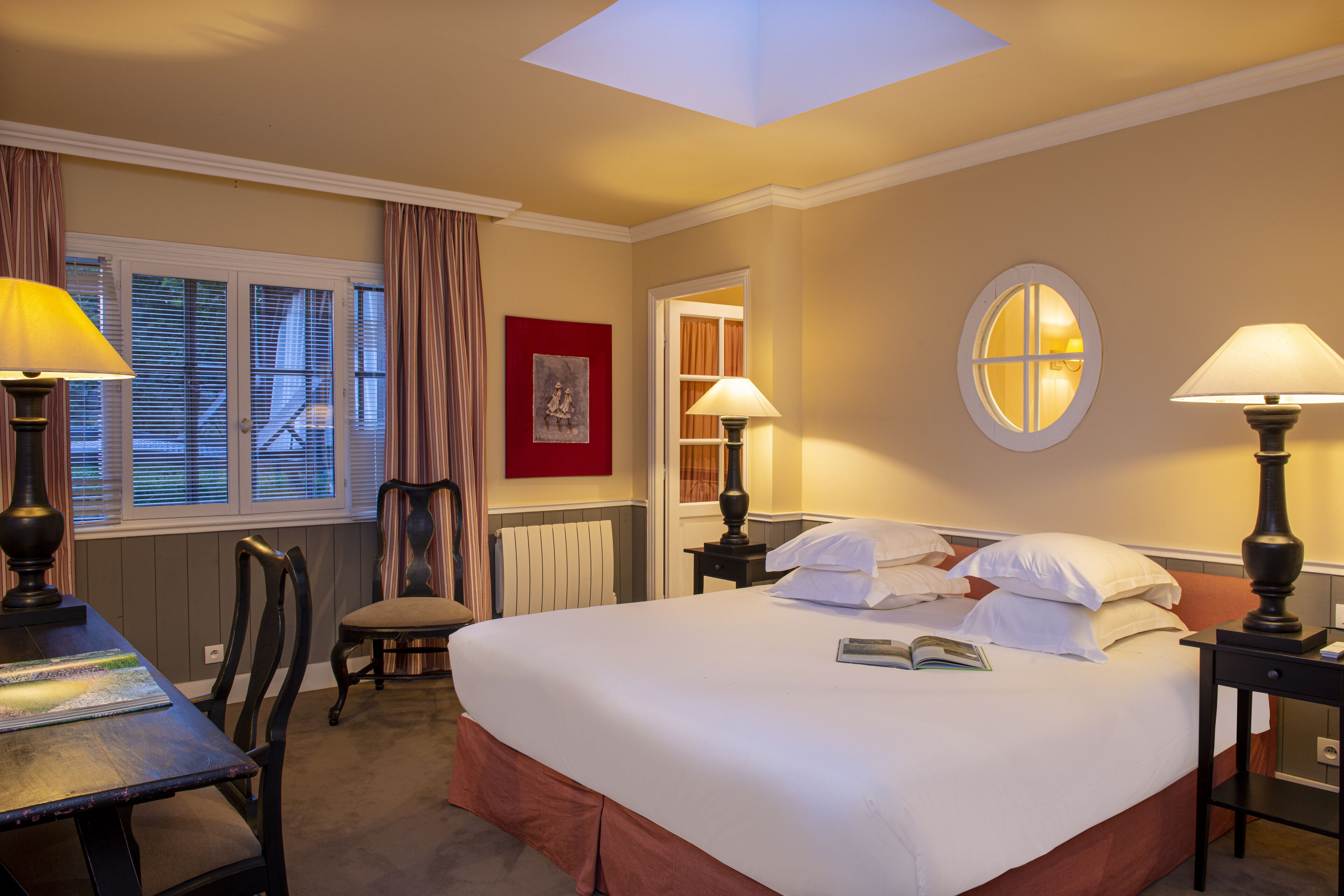 Habitación de hotel con una cama grande, dos mesitas de noche con lámparas, una silla, un escritorio y una ventana con cortinas.