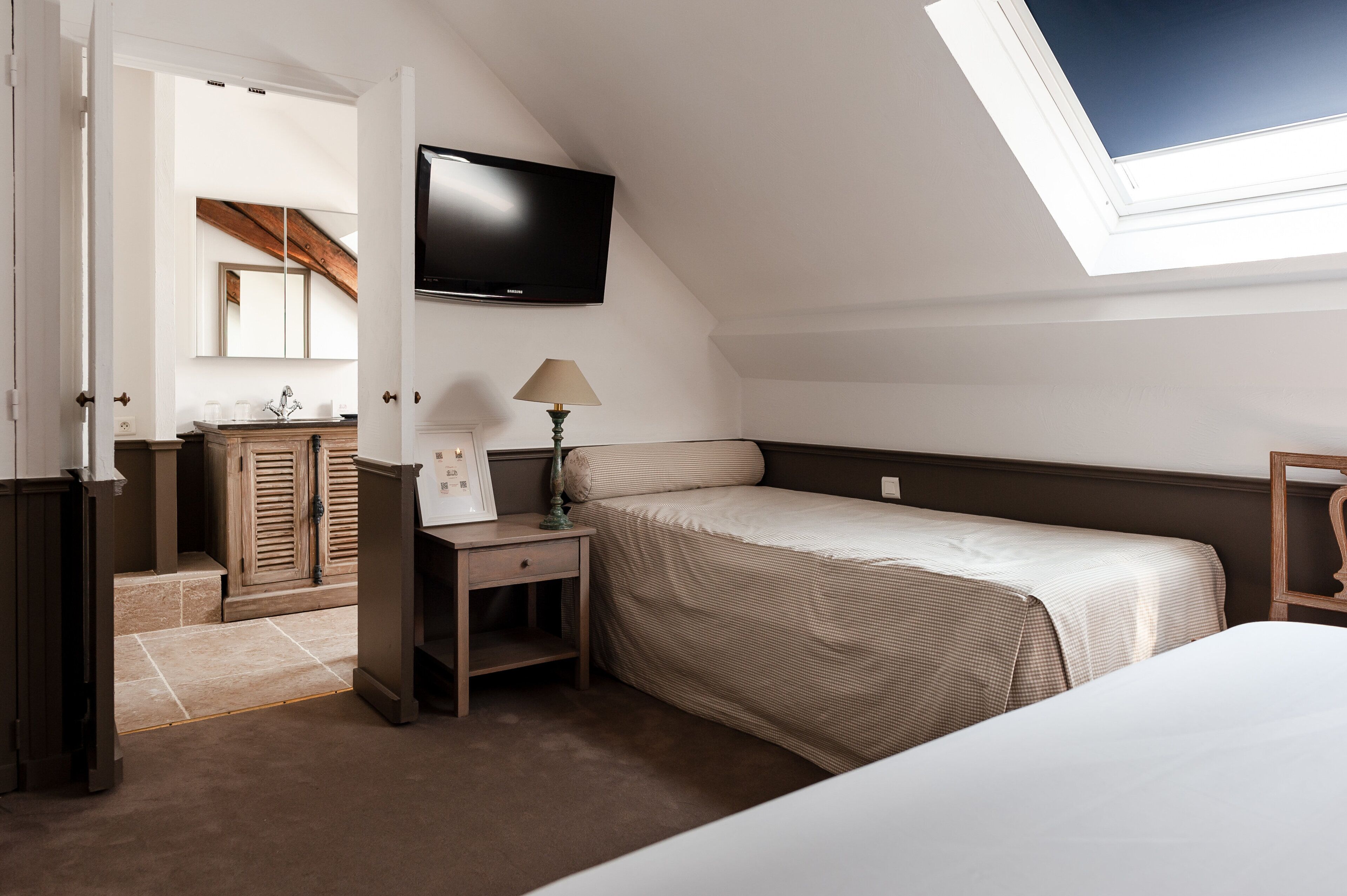 Un dormitorio con cama, escritorio, lámpara, televisor y ventana.