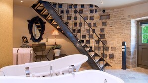 Une salle de bain avec une baignoire sur pieds, un miroir, une chaise et une table avec une lampe.