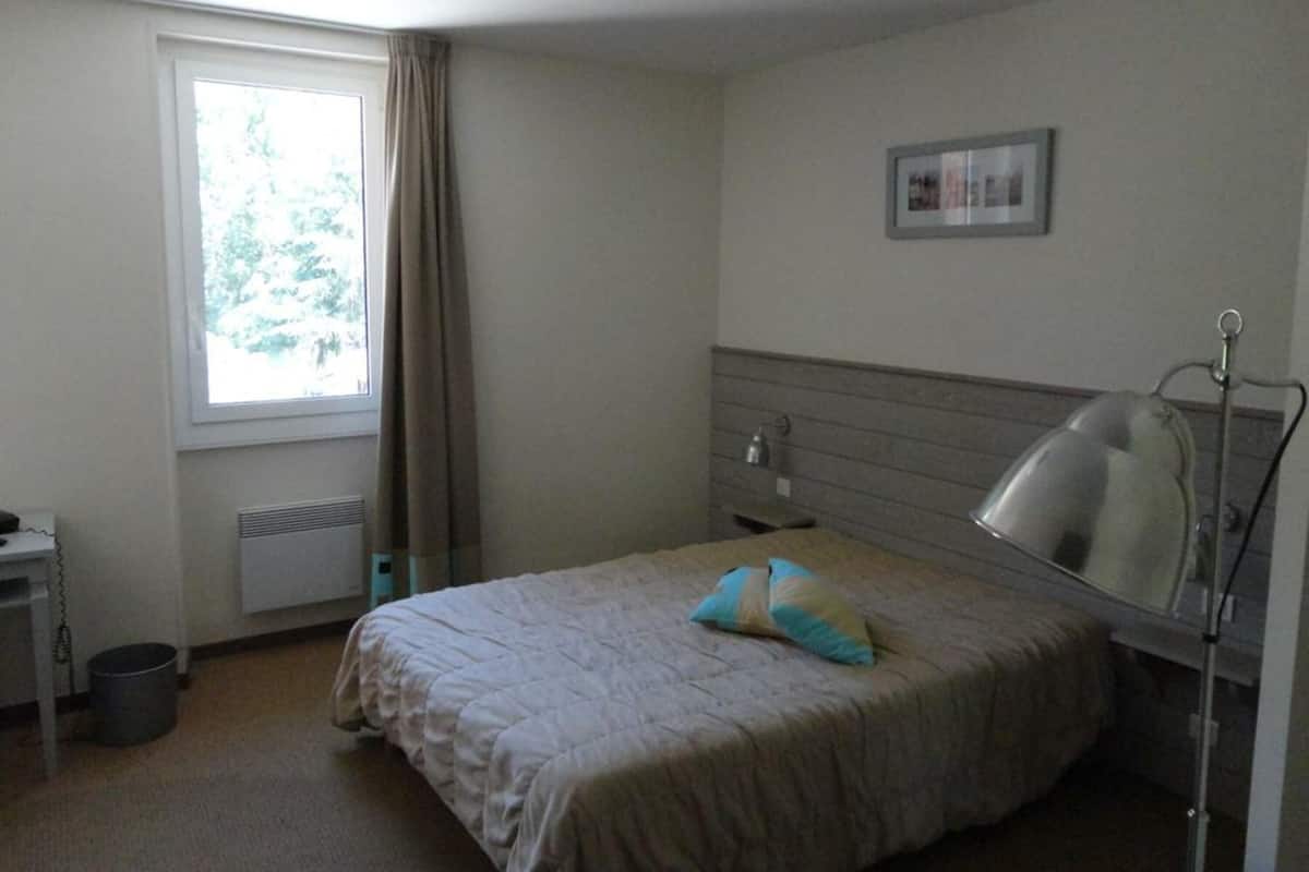 Une chambre à coucher avec un lit, un bureau, une lampe, une fenêtre et un radiateur.