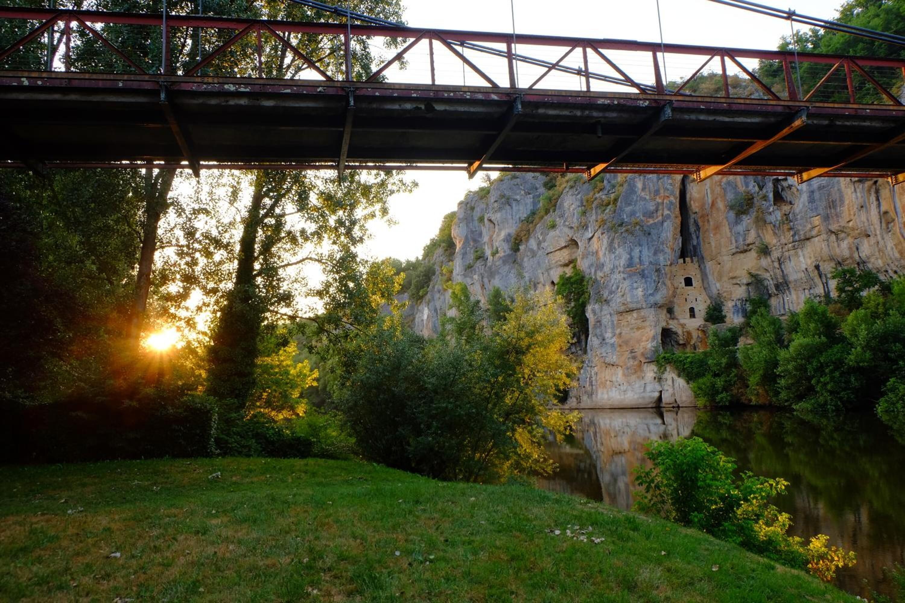 A bridge over a river with a rocky cliff and trees in the background.