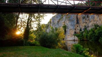 A bridge over a river with a rocky cliff and trees in the background.