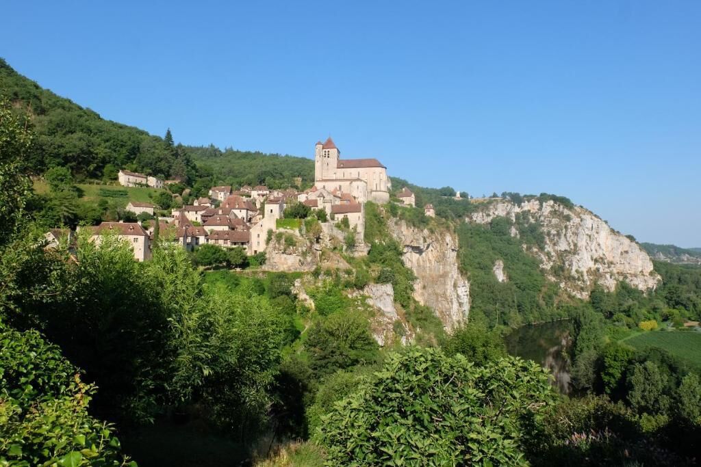 A historic town with a prominent church on a hill, surrounded by lush greenery and a river.
