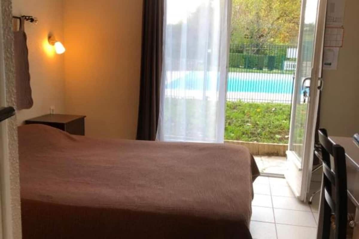 Une chambre à coucher avec un lit, une petite table de chevet, une fenêtre avec des rideaux et une vue sur une piscine.