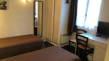 A room with two single beds, a desk with a chair, a television, and a window with curtains.