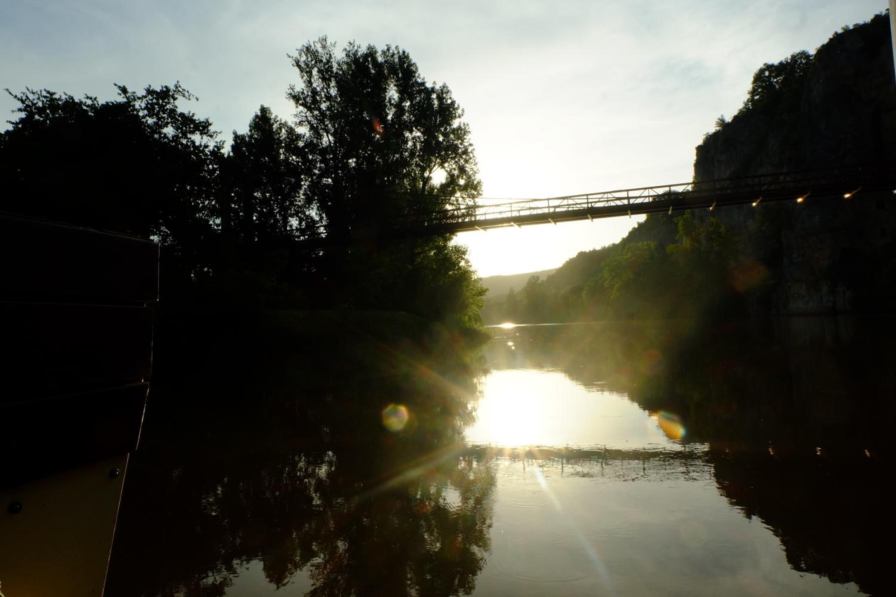 A bridge over a calm river with trees on either side.