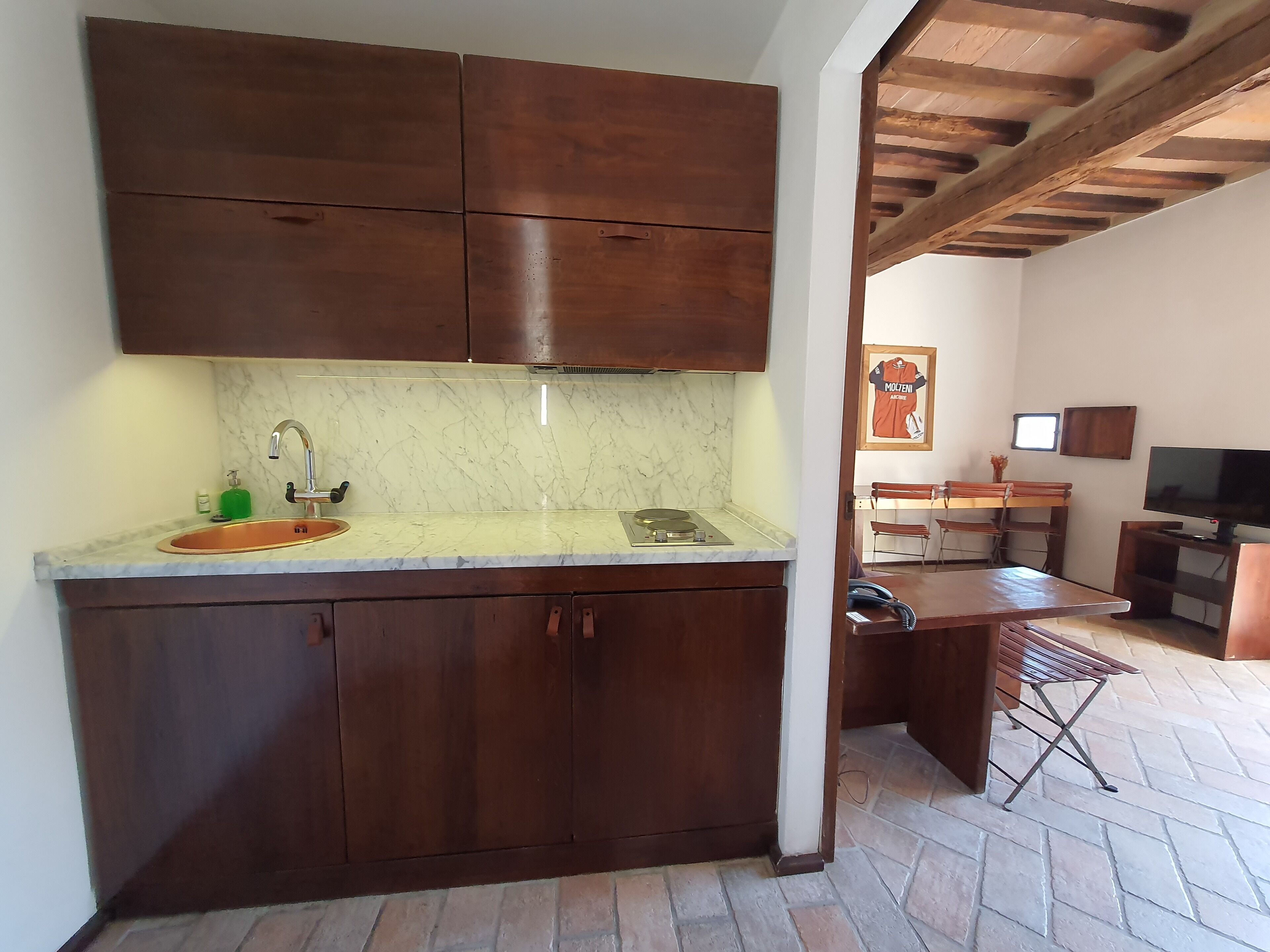 Eine Küche mit dunklen Holzausziehtüren, einer Marmorarbeitsplatte und einem eingebauten Herd. Es gibt einen Essbereich mit Tisch und Stühlen, sowie einen an der Wand befestigten Fernseher.