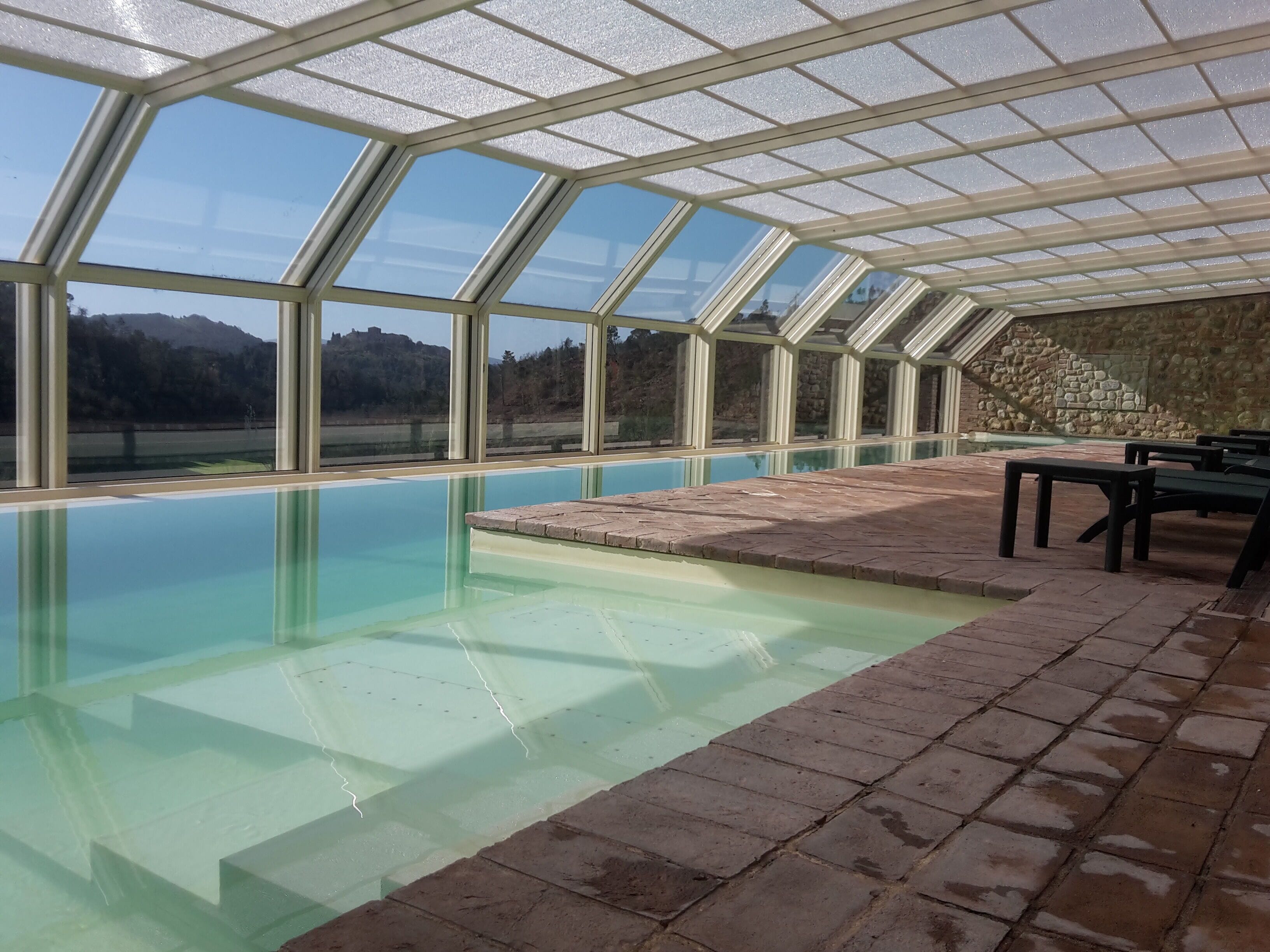 Una piscina con techo de cristal, paredes de piedra y vistas a la montaña.