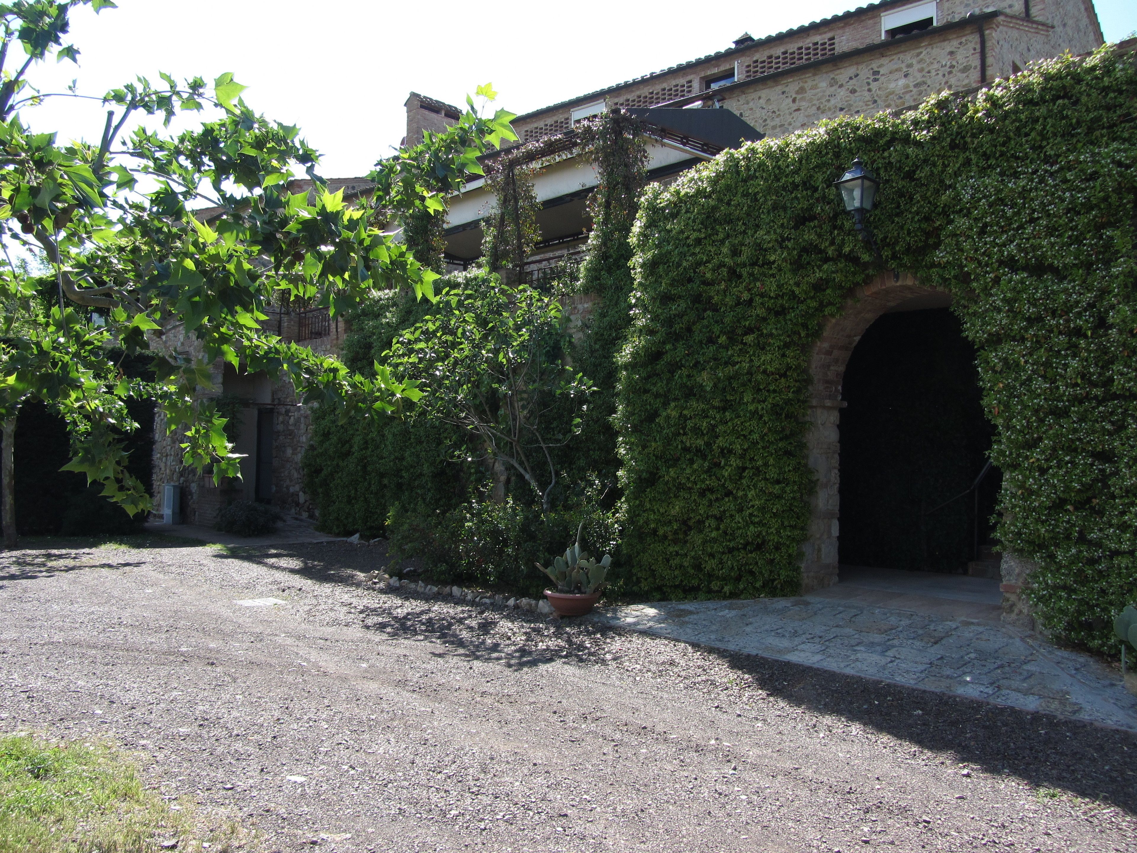 Un patio con un sendero de grava, un muro de piedra cubierto de hiedra y una puerta que da a un edificio.