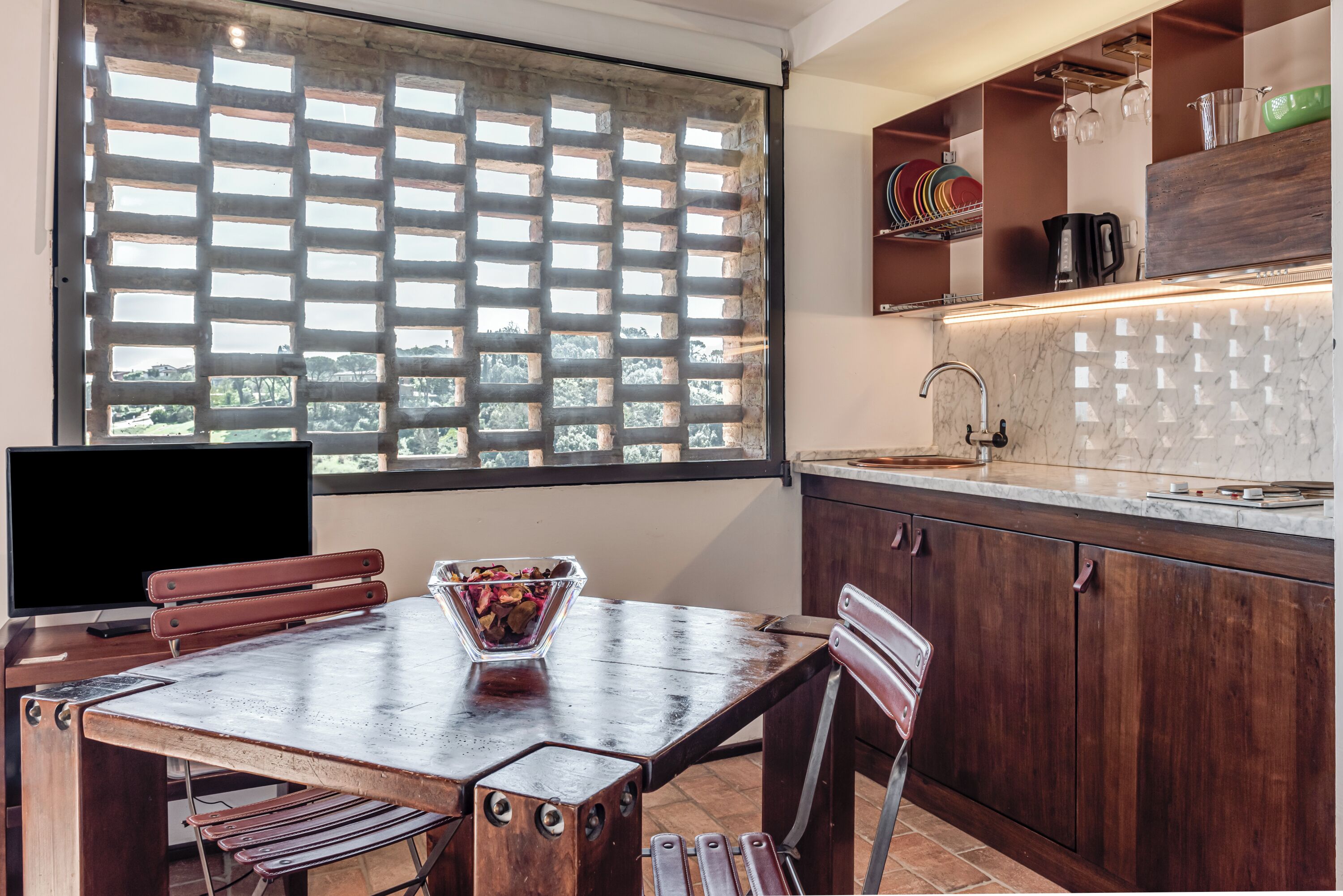 A kitchen with a large window, a dining table with chairs, and a countertop with a sink.
