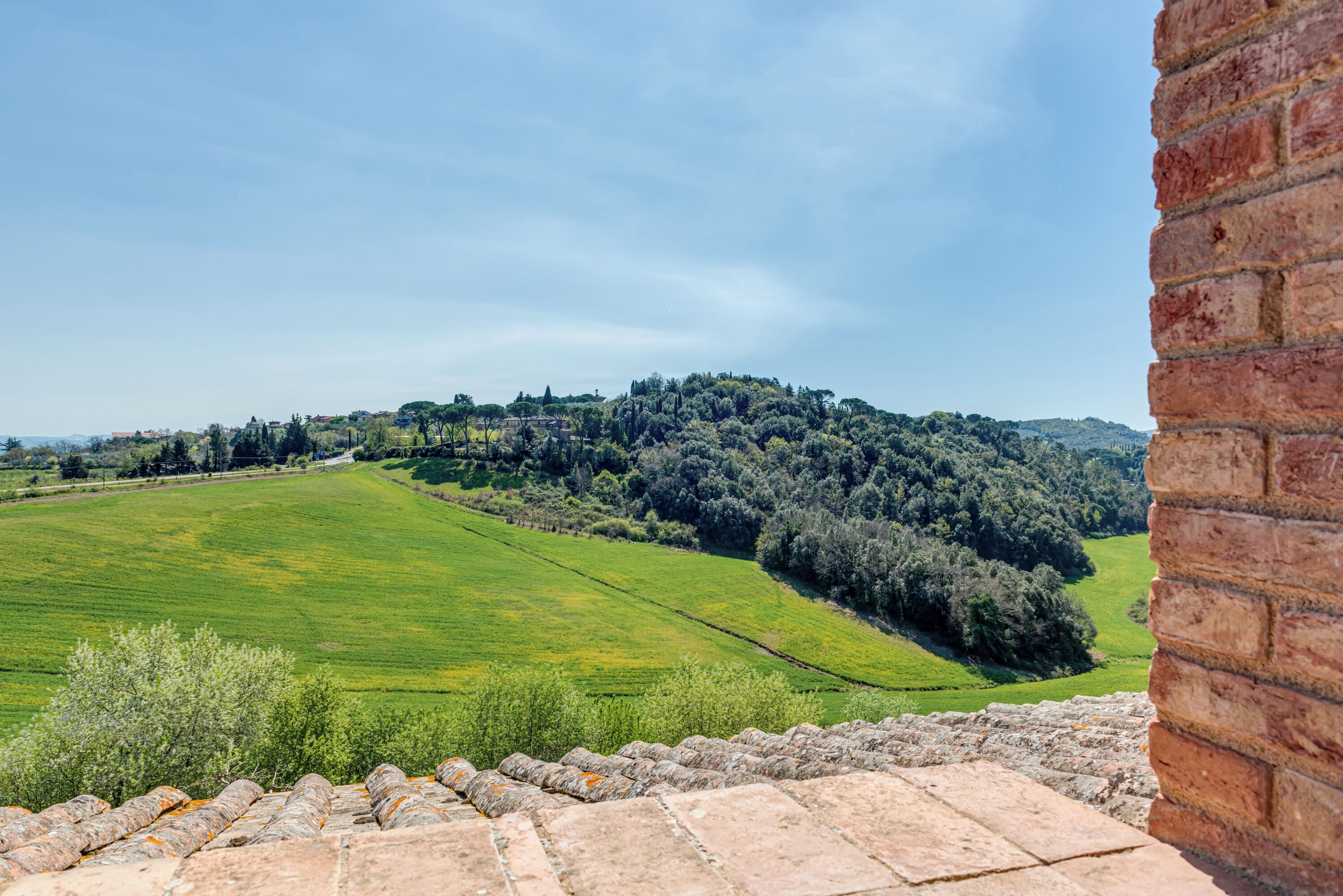A stone wall and a view of a green field with trees and hills in the distance.