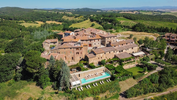 Vista aérea de un complejo histórico de edificios de piedra con piscina, rodeado de abundante vegetación y viñedos.