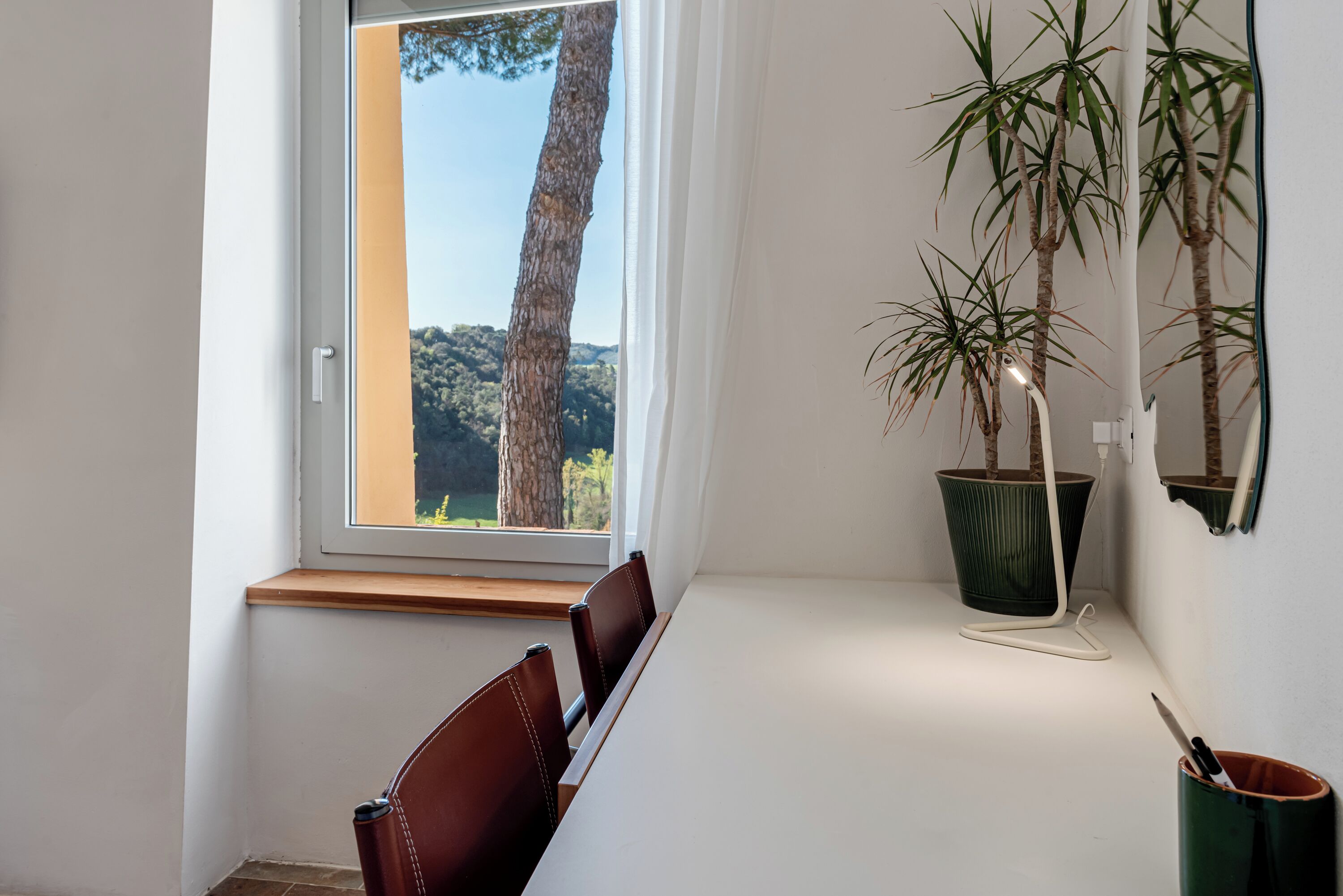 Un área de comedor con una mesa, sillas, un ventanal con vistas a árboles y una planta en maceta.