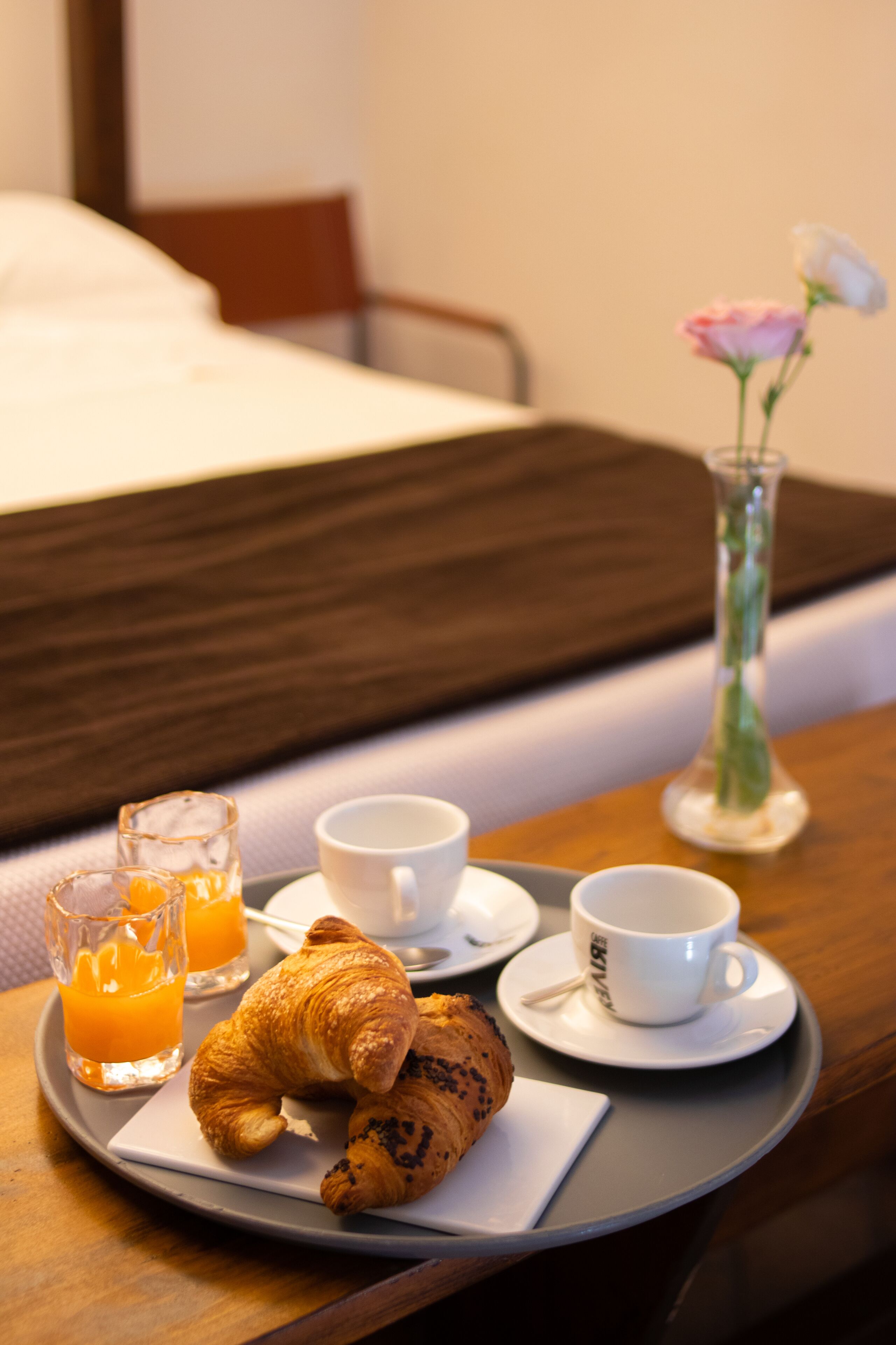 Bandeja de desayuno con cruasanes, jugo y café sobre una mesa de madera en una habitación de hotel.
