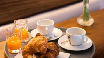 Bandeja de desayuno con cruasanes, jugo y café sobre una mesa de madera en una habitación de hotel.