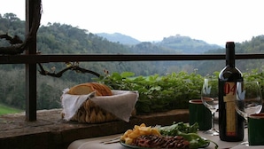 Una mesa dispuesta con una botella de vino, copas y un plato de comida, con vistas a un paisaje montañoso.