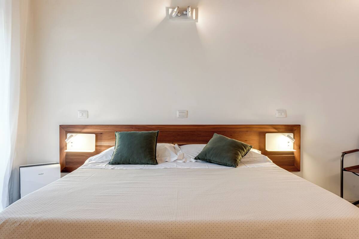 A neatly made bed with a wooden headboard, two bedside lamps, and a nightstand with a lamp.