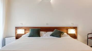 Una cama bien tendida con cabecera de madera, dos lámparas de noche y una mesita de noche con lámpara.