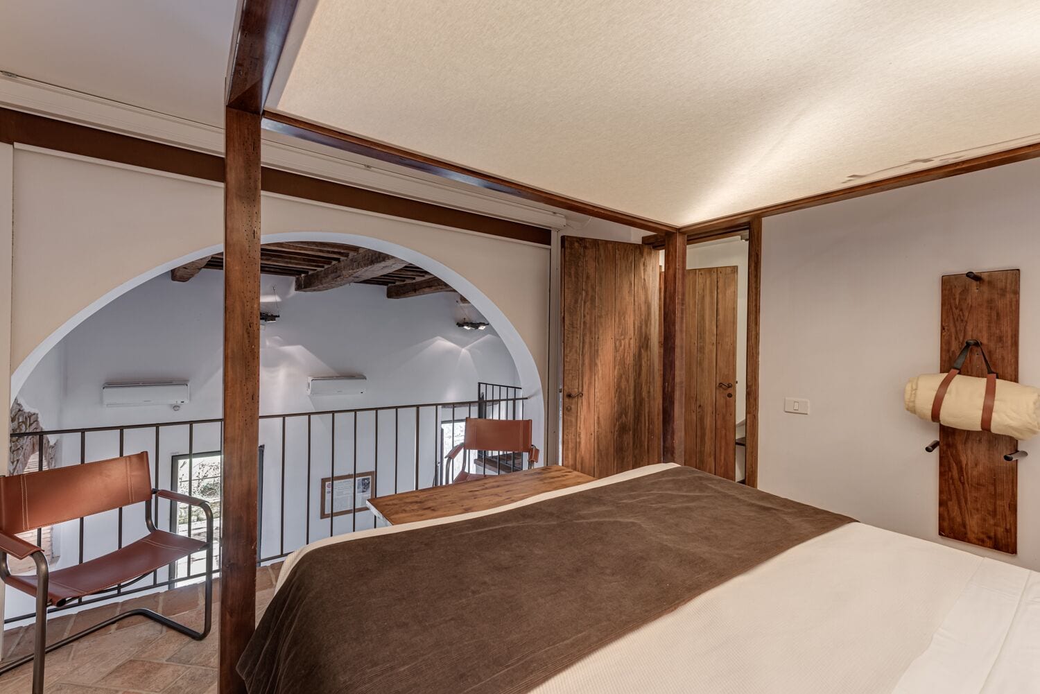 A bedroom with a bed, a wooden desk, a chair, and a balcony with a view.