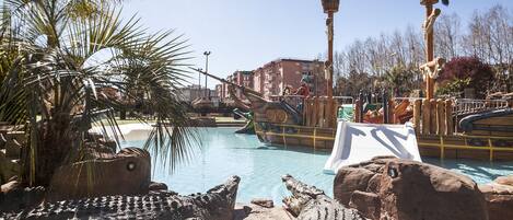 A pool area with large crocodile sculptures, palm trees, and a water slide.