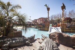 A pool area with large crocodile sculptures, palm trees, and a water slide.